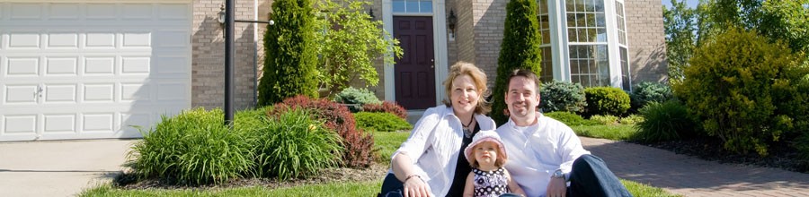 Young family sitting on lawn in front on their home